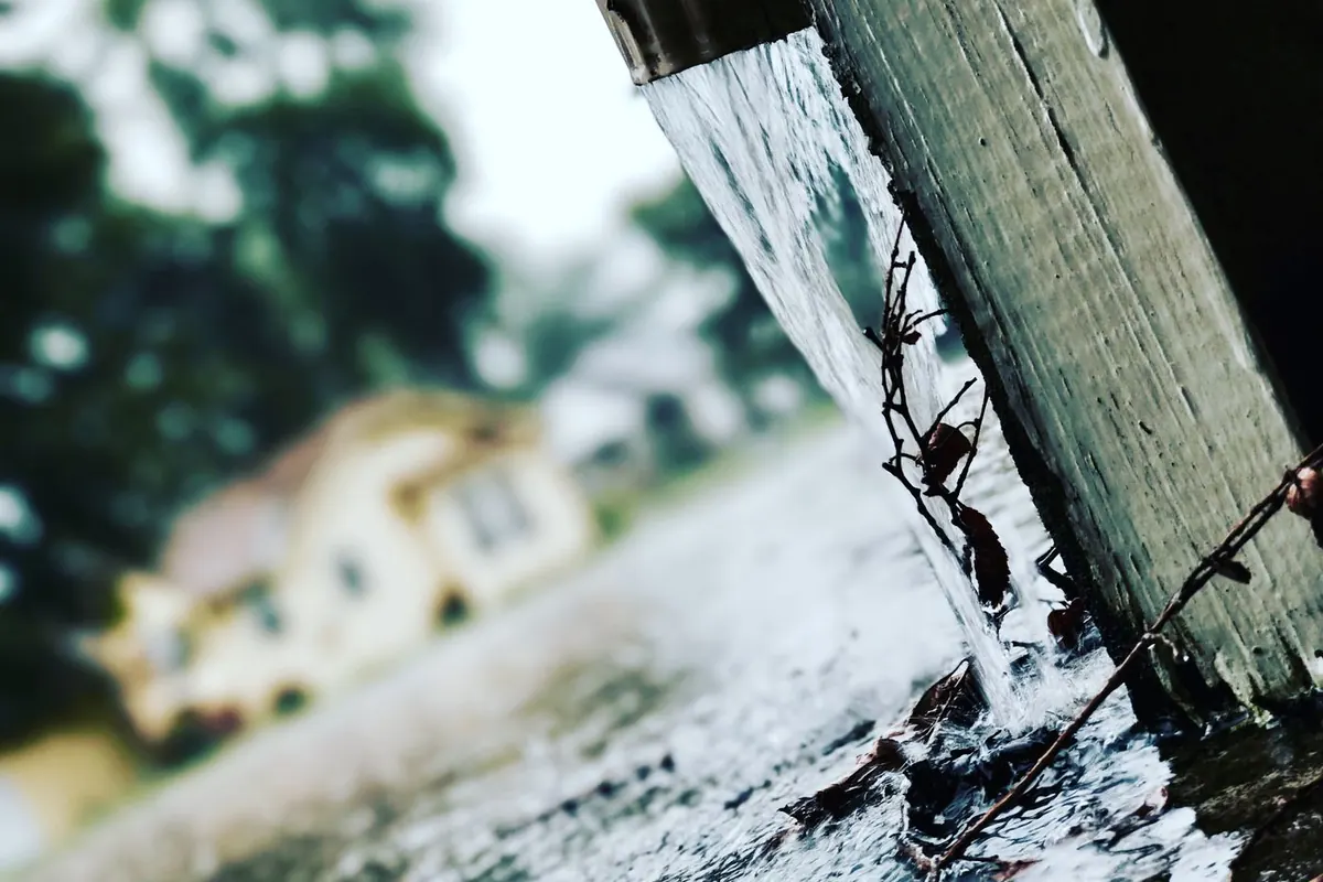 Rainwater pouring off the end of a roof gutter during a storm