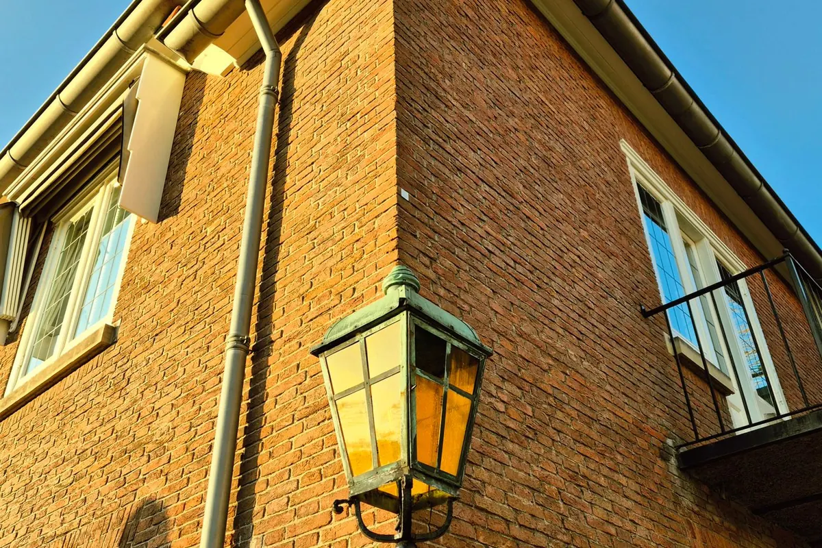 Corner of a brick house with a metal gutter and downspout lit by a lantern