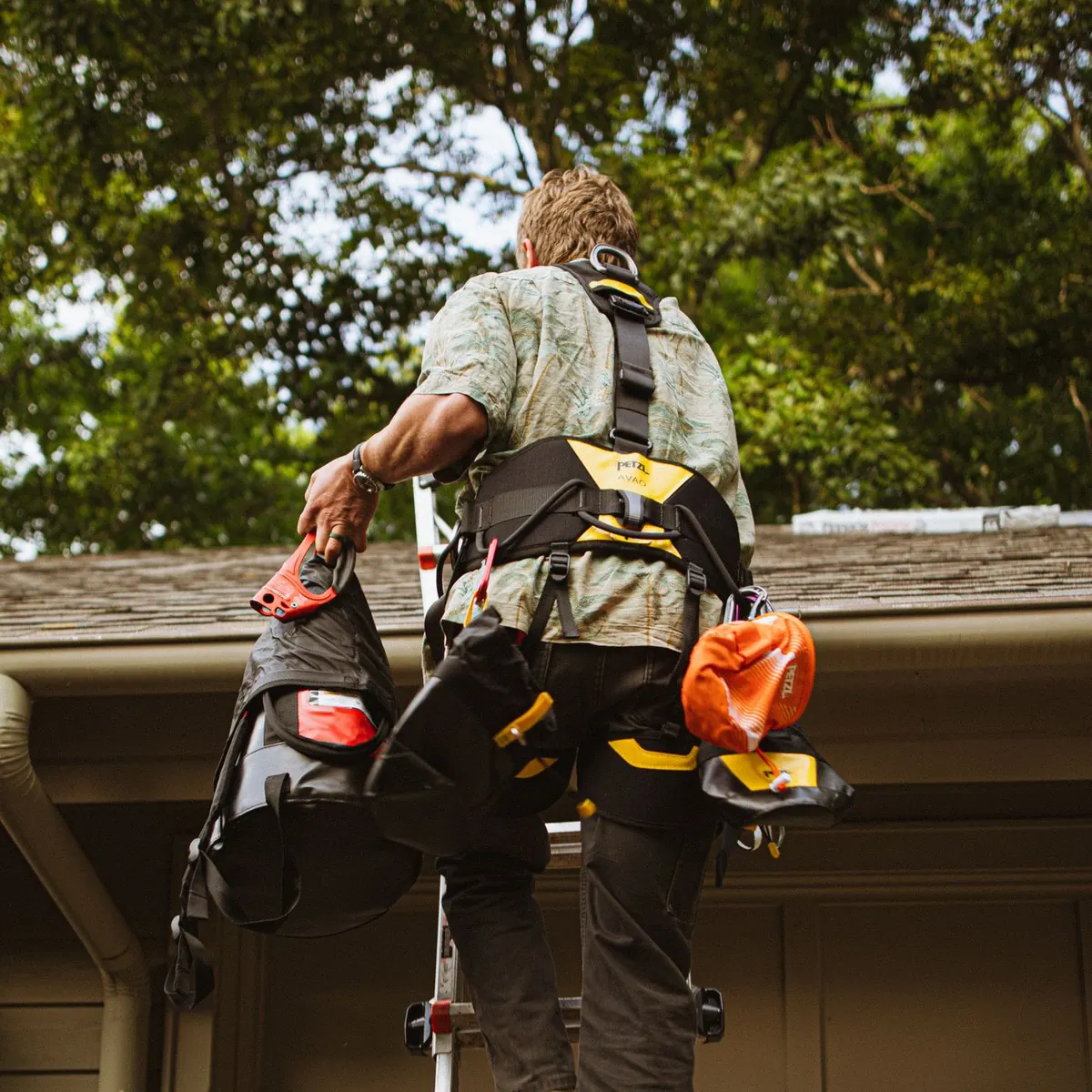 Installer in a safety harness climbing a ladder to the gutter line of a house