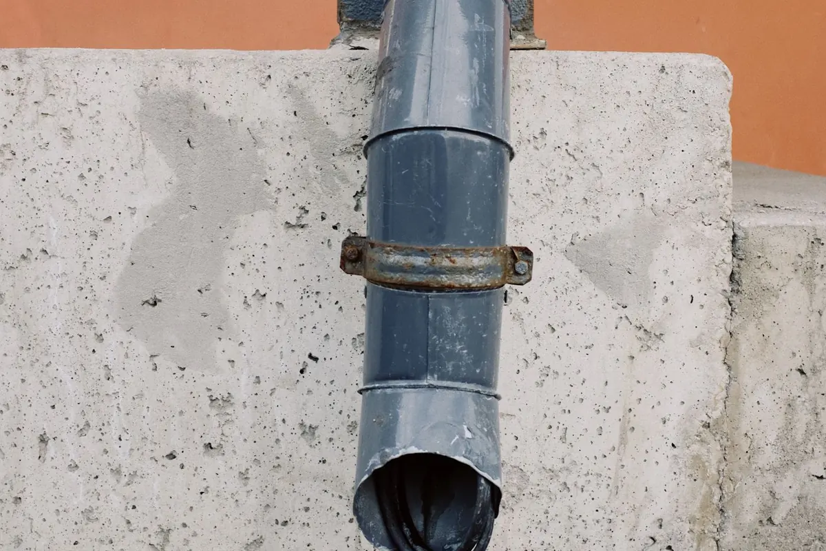Downspout dripping onto paving stones at the base of a wall