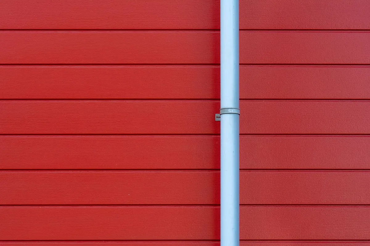 Smooth white downspout running down a red clapboard wall